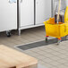 A yellow mop and bucket sitting on a white floor near a Regency stainless steel floor trough.