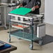 A person using a Metro Prepmate MultiStation on a table in a professional kitchen to hold a green cutting board.