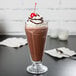 A glass of Ghirardelli dark chocolate milkshake with whipped cream and a cherry.