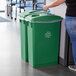 A woman putting a plastic bag into a green Lavex recycle bin with bottle, can, and paper lids.