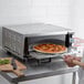 A man putting a pizza into a Waring countertop pizza oven.