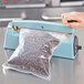 A person using an Omcan manual impulse bag sealer to seal a bag of coffee beans.