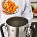A chef pouring a bowl of cut up squash into a stainless steel food blender.