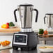 An AvaMix stainless steel commercial food blender on a counter with bowls of cut up pumpkin, soup, and a green bell pepper.