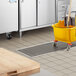 A yellow mop and bucket in a school kitchen with a stainless steel floor trough.