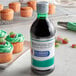 A bottle of McCormick Culinary green food color next to cupcakes with pink frosting.