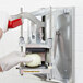 A person using a Vollrath InstaCut 5.1 machine to cut a white onion with a red caution label.