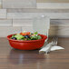 A Fiesta medium scarlet china bowl filled with salad on a table with a water glass and a fork.