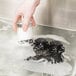 A hand using a black Noble Products glass washer brush in a sink full of water to wash a glass.