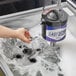A hand using a Noble Products glass washer brush to clean a glass in a sink.
