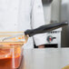 A person in a white coat using a Vollrath black perforated oval spoodle to serve red sauce.