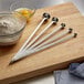 Vollrath stainless steel long handled measuring spoons on a wooden cutting board with a bowl of flour.