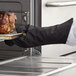 A person in a SafeMitt oven mitt holding a tray of cooked meat.