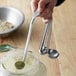 A person holding a Vollrath stainless steel measuring spoon with green powder in it.