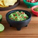 A black Choice Thermal Plastic molcajete bowl filled with guacamole and chips.