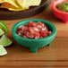 A green Choice Thermal Plastic Molcajete bowl filled with green salsa on a table in a Mexican restaurant.