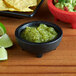 A black Choice Thermal Plastic molcajete bowl of guacamole and chips on a table.