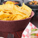 A large round raspberry polyethylene basket filled with tortilla chips on a table.