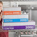 A woman standing behind a stack of Choice 24" x 2000' Foodservice Film boxes.