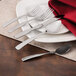 A white plate with a Walco stainless steel knife on it, with silverware and a red napkin.