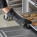 A person in a black SafeMitt taking cookies out of an oven.