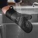 A person washing a black silicone oven mitt in a sink.