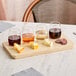 An Acopa wooden flight tray with four stemless wine glasses filled with wine on a table with cheese and meat.