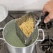 A person using a Vollrath stainless steel pasta basket to strain spaghetti over a pot of water.