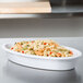 A white oval melamine casserole dish filled with pasta and vegetables on a counter.
