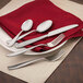 A Walco stainless steel teaspoon on a red napkin with silverware.