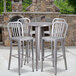 A Flash Furniture silver metal bar height table with four chairs with vertical slat backs on an outdoor patio.