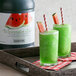 A green watermelon slushy in a glass with straws.