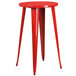 A red round metal bar height table with red metal stools with vertical slat backs.