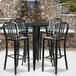 A Flash Furniture black metal bar height table with four black metal stools with vertical slat backs on an outdoor patio.