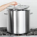 A hand using a Vollrath stainless steel lid to cover a large pot.