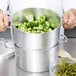 A person holding a Vollrath Wear-Ever steamer pot with broccoli and green beans.