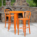An orange metal bar height table with two orange chairs on an outdoor patio.