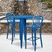 A blue metal bar table with two blue chairs in front of a stone wall.