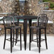 A Flash Furniture black metal bar table with four black metal chairs with black seats on a stone wall patio.