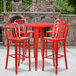 A red metal bar table with four red chairs on an outdoor patio.