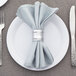 An American Metalcraft aluminum napkin ring on a white napkin on a white plate.
