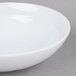 An Arcoroc white soup/cereal bowl with a rim on a gray surface.
