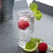 A Stolzle shot glass of ice water with raspberries and mint leaves.