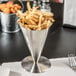 A Tablecraft stainless steel footed french fry cone filled with french fries on a table.