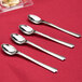 A close-up of four WNA Comet Reflections stainless steel look plastic tasting spoons.