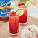 A glass of red Torani raspberry limeade garnished with a lime wedge and raspberries.