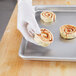 A hand in a white glove holding a cinnamon roll on a Chicago Metallic aluminum sheet pan.