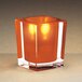 A Sterno orange and clear square liquid candle holder with a light inside holding a small orange candle.
