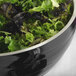 A black Vollrath Double Wall metal serving bowl filled with green and black lettuce.