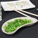 A Tuxton eggshell china crescent dish with seaweed salad and chopsticks on a table.